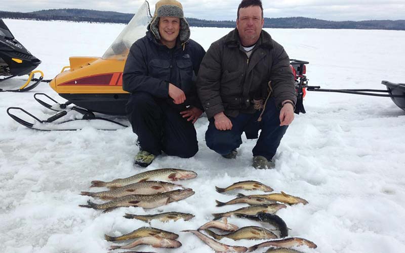 Deux hommes posant devant les poissons qu'ils ont pêché sur un lac gelé